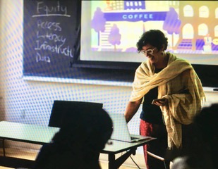 Greta Byrum leading a workshop in a classroom, beside a chalkboard listing equity, access, literacy and infrastructure